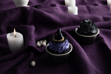 delicious Halloween cupcakes near burning candles on purple cloth