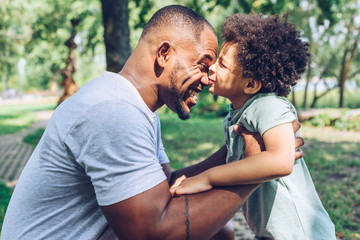 Fototapeta premium cute african american boy kissing happy father while having fun in park