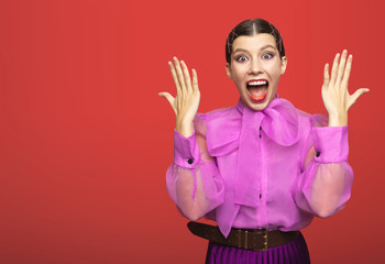 girl actress posing with positive emotion. in the Studio on a red background. the girl is surprised and shows her hands