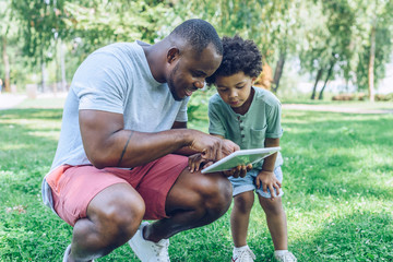 handsome african american man using digital table with cute son in park
