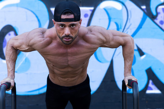 Fitness man training calisthenics without shirt on the street. He  is using parallel bars to do push-ups