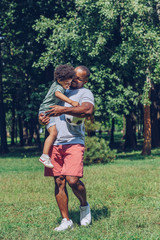 Fototapeta premium happy african american boy holding soccer ball while sitting on fathers hands