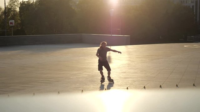 Young long-haired bearded man roller skater is dancing between cones in the evening in a city park at sunset. Freestyle slalom Roller skating between cones.