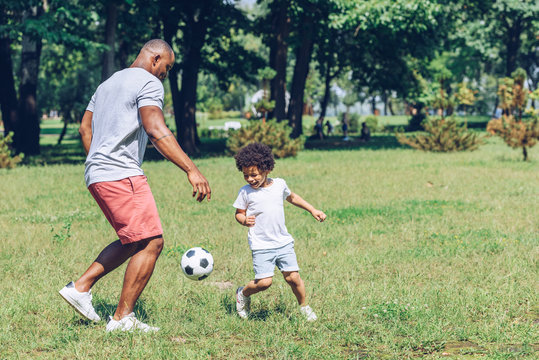 young african american father playing football with cute son in park