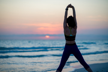 active sports woman on ocean shore in evening stretching