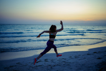 fit sports woman on ocean shore in evening jogging