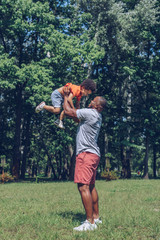 happy african american man holding cheerful son above head while having fun in park