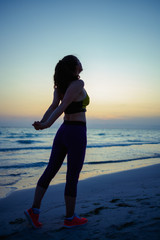 fit woman in sport clothes on seashore in evening stretching