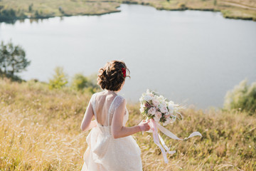 Fototapeta na wymiar Modern bridal style. Caucasian bride walking outdoors holding a beautiful bouquet of colorful fresh flowers in her hands.