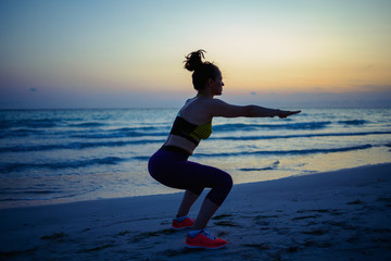 fitness sports woman on beach in evening doing squats