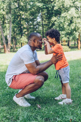 cheerful african american boy having fun with happy father in park