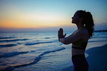 young woman on ocean shore in evening meditating