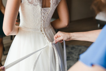 Obraz na płótnie Canvas Modern bridal fashion. Closeup of bridesmaid tying bow on bride's dress.