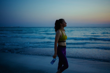 sports woman with water relaxing on ocean shore in evening