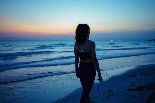 young woman with bottle of water walking after workout