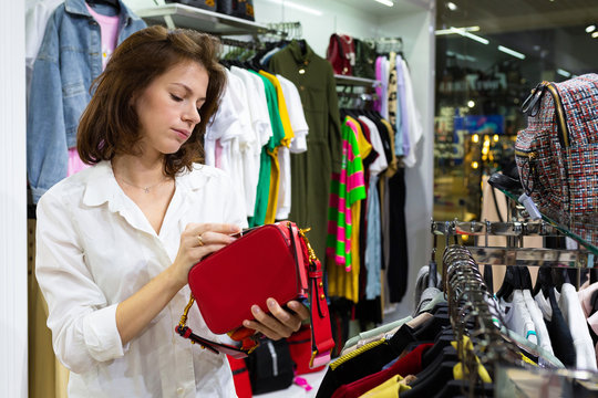 The girl chooses a red clatch in the store.