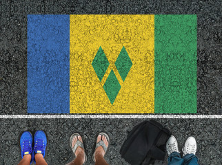 people legs are standing on asphalt road next to flag of  Saint Vincent and the Grenadines and...