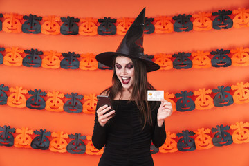 Image of witch girl in halloween costume holding phone and credit card