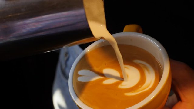 Barista girl pours draws milk over a coffee - making latte art for cappuccino