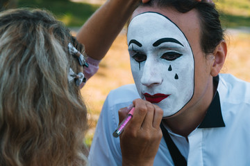 Girl paint lips to young man mime with red pencil