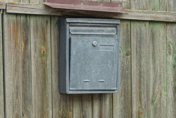 one gray metal mailbox hanging on a green wooden fence