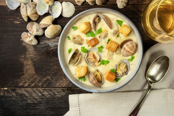 Clam chowder with fresh parsley and croutons, with shells and a glass of white wine, shot from the top on a dark rustic wooden background with a place for text