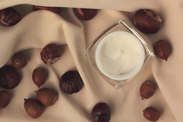 Flat lay with a moisturiser in a glass jar surrounded by chestnuts and acorns. Concept of fall skincare.
