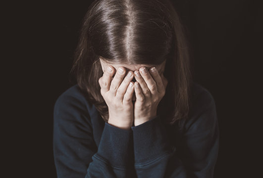 Portrait of a crying woman covering her face with hands on a black background. Violence in family. Sadness and depressive state of the girl.