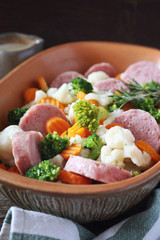 Steamed vegetables (carrots, cauliflower, broccoli) and sausage in ceramic bakeware
