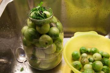 Large glass jar with green tomatoes stands in sink