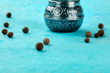 Allspice, Jamaica pepper. Black peppercorns with a vintage pepper mill, close-up on a blue...