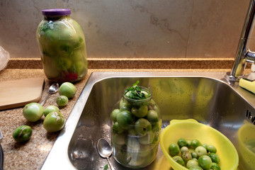 Large glass jars with green tomatoes stands in  kitchen
