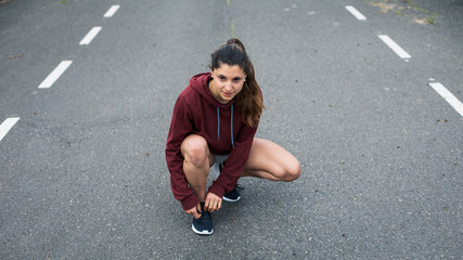 Motivated female athlete lacing running shoes and gettting ready for training on asphalt road.