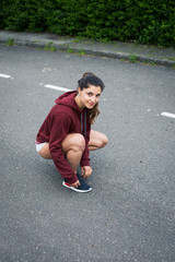 Confident female athlete lacing running shoes and gettting ready for training on asphalt road.