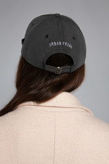 Medium close-up back shot of brown-haired lady in a beige jacket and a gray cap with an embroidered...