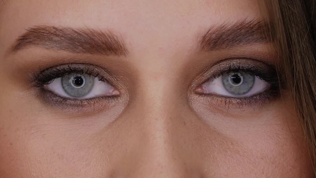 Eyes of young woman with professional ringlight makeup looks straight into the frame and closes her eyes slow motion. Beautiful girl with blue eyes close-up circular light