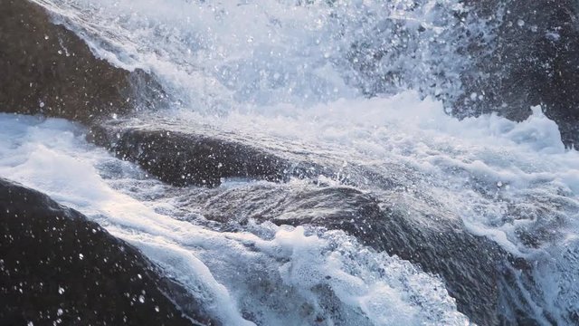 A close up shot in super slow motion of a rapid stream of water hitting a big rock and creating a big splash. Soft and nice light in the sunset. Nature in Norway.