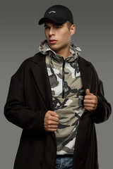 Medium close-up shot of a short-haired European man dressed in a dazzle hooded top, a black jacket and a black baseball cap with an embroidered black lettering "New York".