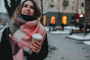 Thoughtful young woman in warm clothing standing on city street during winter