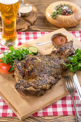 roasted lamb leg with fresh vegetables on wooden board and glass of beer on wooden table