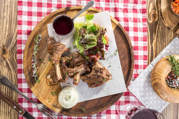 Grilled lamb ribs with green mix and honey sauce on wooden board and glass of red wine on wooden table