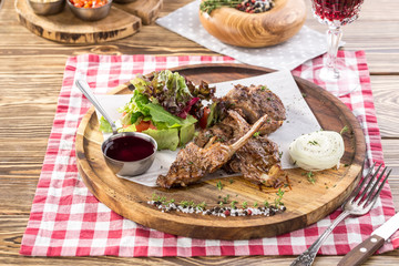 Grilled lamb ribs with green mix and honey sauce on wooden board and glass of red wine on wooden table