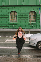 Happy young woman in warm clothing crossing city street in winter