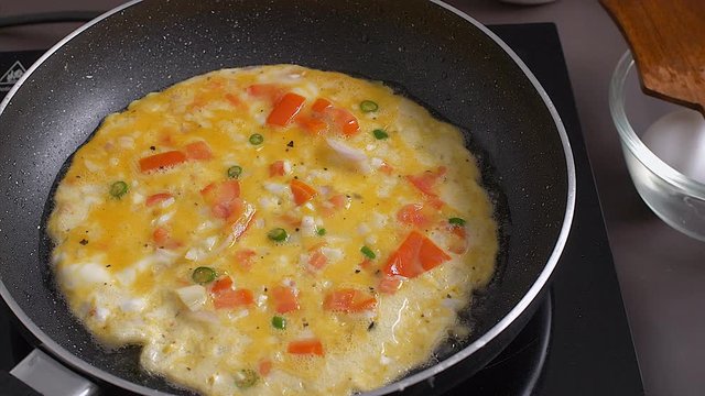 Fresh omelette is getting cooked on a frying pan. 