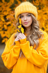 Beautiful girl walking outdoors in autumn. Smiling girl collects yellow leaves in autumn. Young woman enjoying autumn weather.