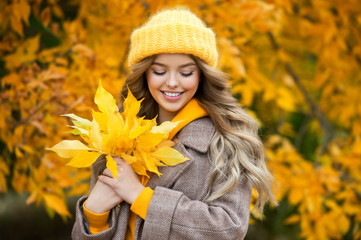 Beautiful girl walking outdoors in autumn. Smiling girl collects yellow leaves in autumn. Young woman enjoying autumn weather.