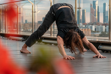 Attractive athletic man practicing yoga in business center with beautiful view on a city from skyscraper.