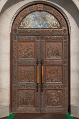 Fototapeta na wymiar Wooden arched door of church with engraving of the scenes from Bible and stained glass