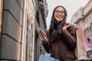 Asian woman using smartphone and looking away while enjoying a day shopping
