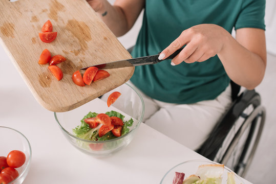 partial view of disabled woman adding sliced tomatoes in glass bowl in kitchen